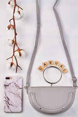 Branch of white cotton near fashionable things. Stylish leather bag and marble phone case on white background.