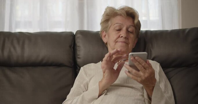 An elderly woman after retirement cut short hair with light brown hair Lie on the sofa and enjoy social media on her smartphone at her home alone restlessly.