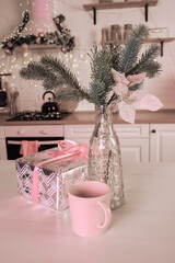 composition in pink tones from a vase with a spruce branch, a cup and a New Year's gift, against the background of a decorated kitchen