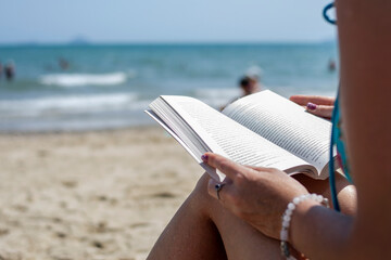 Woman reading a book on the beach, blurred background. Summer leisure on the beach