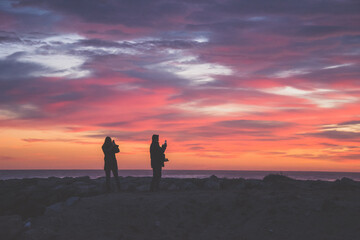 Silueta de personas con c&aacute;maras y smartphones haciendo fotos al mar en el atardecer.