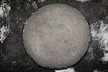 Black round slate board on dark stone texture top view. Place for a menu or recipe