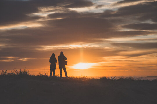 Silueta de pareja delante del mar. Fot&oacute;grafo fotografiando el atardecer 