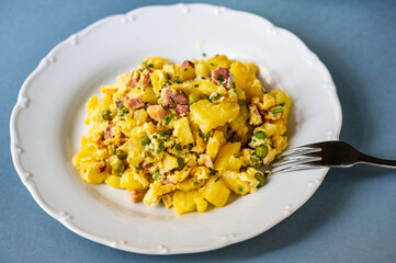 Scalloped potato with bacon, pea and egg on white plate.