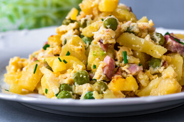 Pile of scalloped potato with peas, bacon, egg and herb on plate.