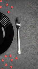 Empty black plate and silverware on black stone table decorated for valentine day