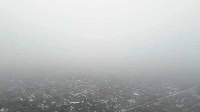 Misty aerial reveal of countryside village housees descending from clouds