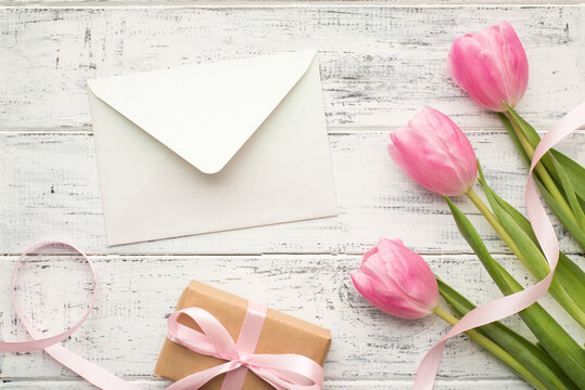 Happy mom's day concept. Overhead flat lay close up view photo picture of three pastel color flowers with wrapped kraft present sulky ribbon and open white envelope on wooden table