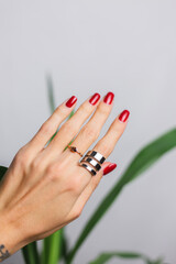 Woman hand with red manicure and two rings on fingers, on beautiful green palm leaf tropical...