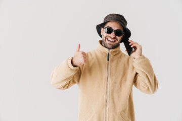 Joyful handsome guy showing thumb up while talking on cellphone