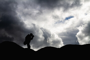 Silhouette of a man in the mountains is taking pictures of the landscape