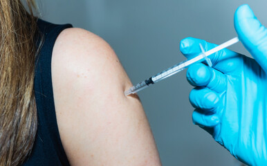 A nurse administers a vaccine, with a shot, by tapping a young woman on the shoulder.