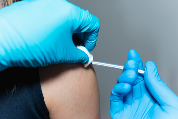 A health care provider administers a vaccine. He gives an injection with one hand while holding a cotton ball in the other hand. He pricks a young woman's shoulder with a syringe.