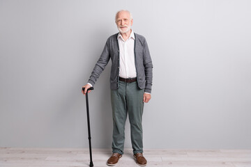 Full size photo of optimistic old man stand with stick wear dark sweater trousers isolated on grey...