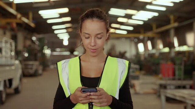 Beautiful african worker American is using a cell phone in a factory workshop, she smiles happily at work.
