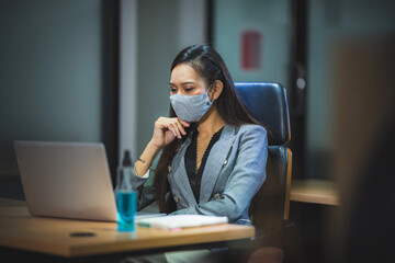 young business person wearing surgical face mask for protection with coronavirus covid-19, working in office with new normal protection lifestyle, social distancing and self-isolated