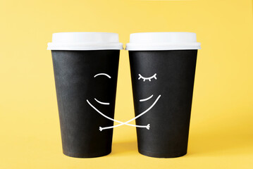 Loving couple of coffee cups. Hugging disposable coffee cups on a yellow background. Creative concept of romantic relationships