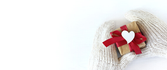 hands in mittens with a gift and a heart symbol. receiving or giving on the holiday of lovers