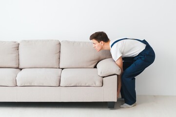 Obraz premium Loader moves sofa, couch. worker in overalls lifts up sofa, white background. Delivery service concept. Courier delivers furniture in case of move out, relocation.