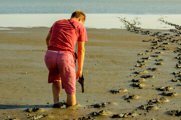 barefoot young man of the European race in a red t-shirt and pink shorts plunge in the mud