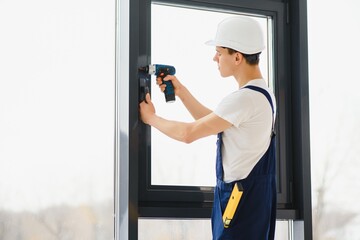 Workman in overalls installing or adjusting plastic windows in the living room at home