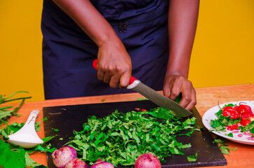 African chef carefully cutting vegetables with knife on the table