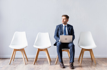 Businessman with laptop sitting on chair in hall