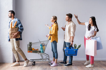Angry multicultural customers with purchases pointing with hands in queue