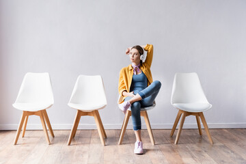 Young woman using headphones while waiting on chair in hall