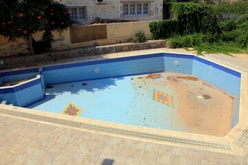 Pool without water, sand and dust, unkempt. On a sunny day, blue tiles with patterns