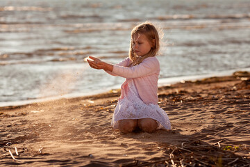 Cute little girl playing with falling sand at the beach in sunset