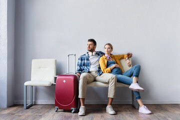 Pregnant woman sitting near husband and suitcase in airport