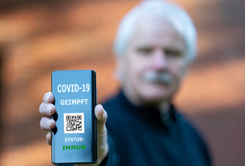 Älterer Herr zeigt digitalen Impfpass auf dem Smartphone, auf dem eine COVID-19 Impfung...