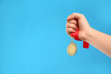 Naklejka na ściany i meble Woman holding gold medal on light blue background, closeup. Space for text
