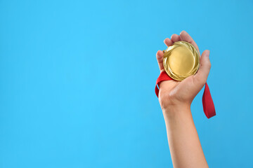 Woman holding gold medal on light blue background, closeup. Space for text