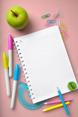 School supplies:notepad,colored markers and pencils,ruler, green apple lie on a red/pink desk. The concept of school children's creativity in trendy colors.