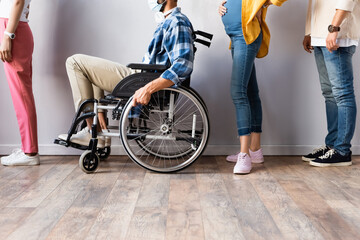 Disabled man in medical mask sitting in wheelchair near pregnant woman in queue