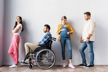 Pregnant woman checking time near disabled man and multiethnic people in hall