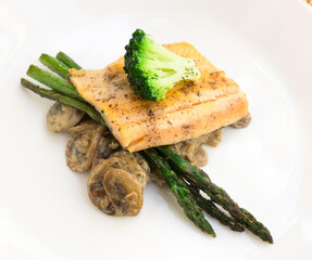 dish of fried river trout fillet with garnish of broccoli, asparagus sprouts and mushroom sauce on white background