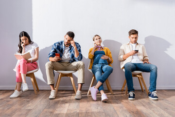 Multiethnic people using smartphones and reading book on chairs in hall