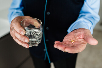 Old man's hands holding pills and glass of water