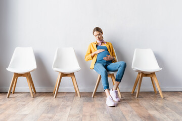 Pregnant woman with hands on tummy sitting on chair in hall