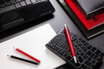 Pocket Organiser, clean sheet of paper, pencils and pen, laptop and office books on black table,top view.  Black and red concept still life for office, business or education