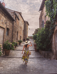 modella con cappello grande e vestito colorato di spalle che passeggia in borgo (civita di...