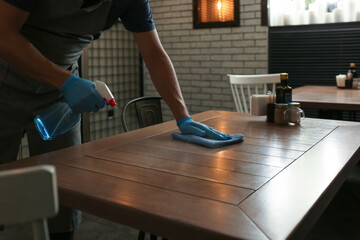 Fototapeta na wymiar Waiter in gloves disinfecting table at cafe, closeup
