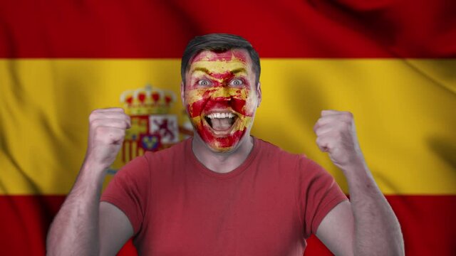 A screaming Spanish cheerleader with a face painted in the color of the Spanish flag.