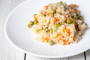 Quinoa porridge with vegetables and avocado in a white flat plate on a wooden board. Superfoods concept and top view.