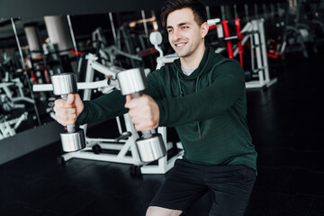 Fototapeta na wymiar Handsome male athlete squats with dumbbells in modern gym. Healthy Lifestyle