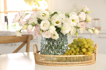 Obraz na płótnie Canvas Bouquet of beautiful eustoma flowers and grapes on white table in kitchen. Interior design