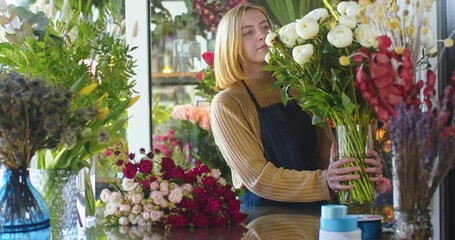 Medium shot of female florist making blossom bouquet. Woman putting flowers in table and looking on them smiling. Designing, floral workshop, working during pandemic concept.